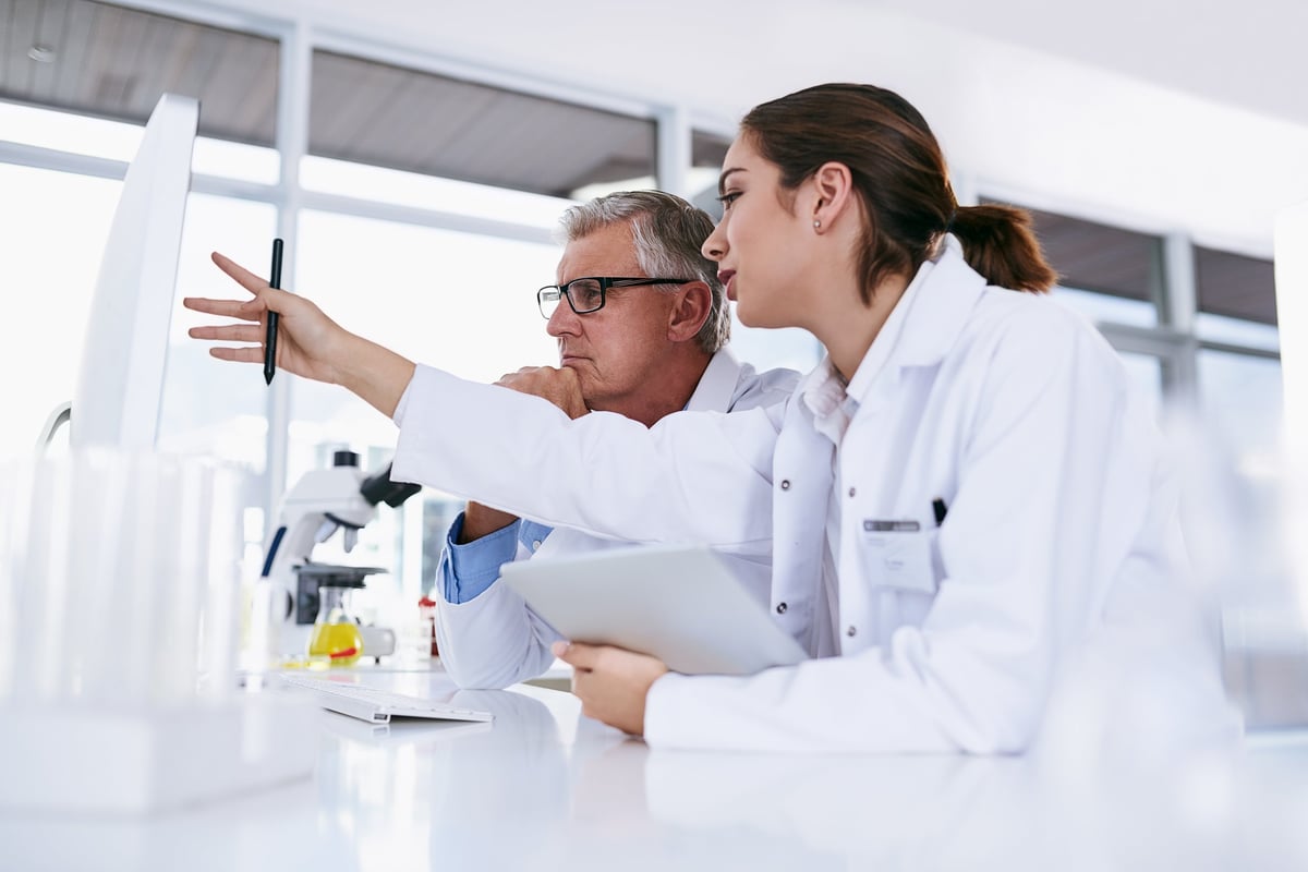 Two scientists collaborating at a computer in a modern laboratory with clean white counters and professional equipment